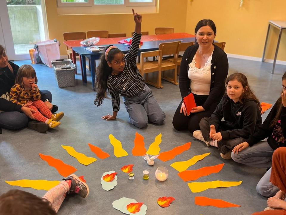 Im Kindertreff schauen sich die Kinder mit Marina Novosel ein Bild zu Pfingsten an, auf dem der Heilige Geist die Jünger erleuchtet.