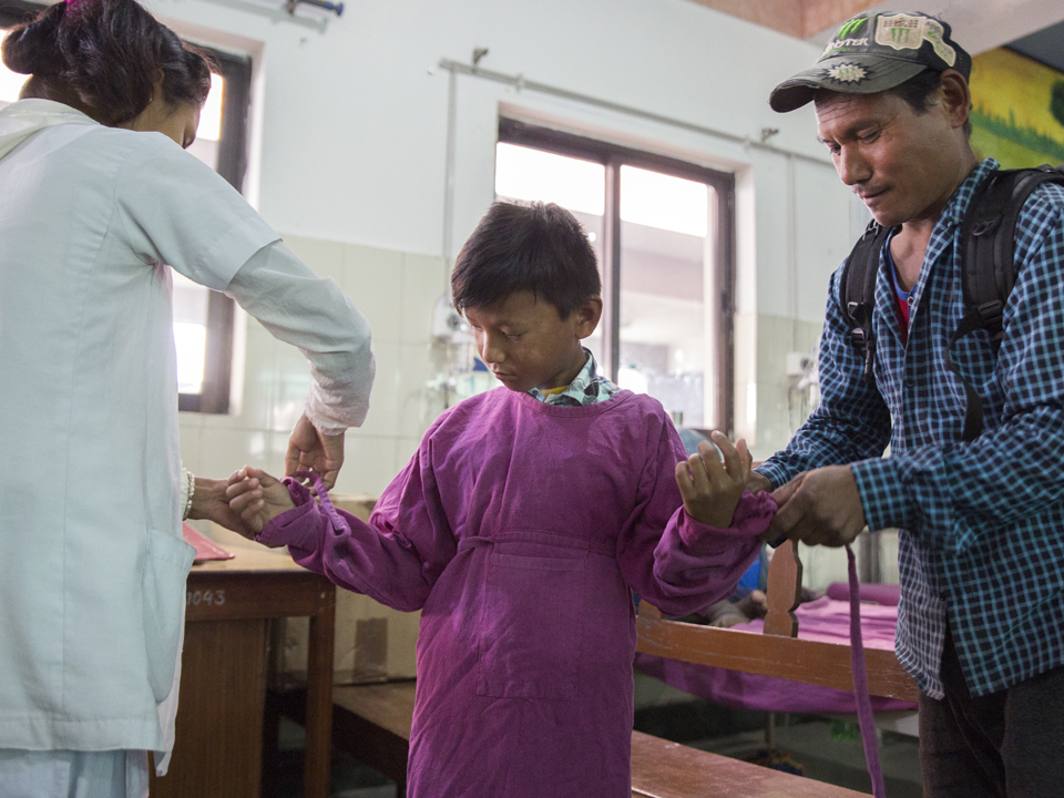 Eine Krankenschwester und Dipendras Vater helfen ihm, sich für die bevorstehende Operation vorzubereiten.