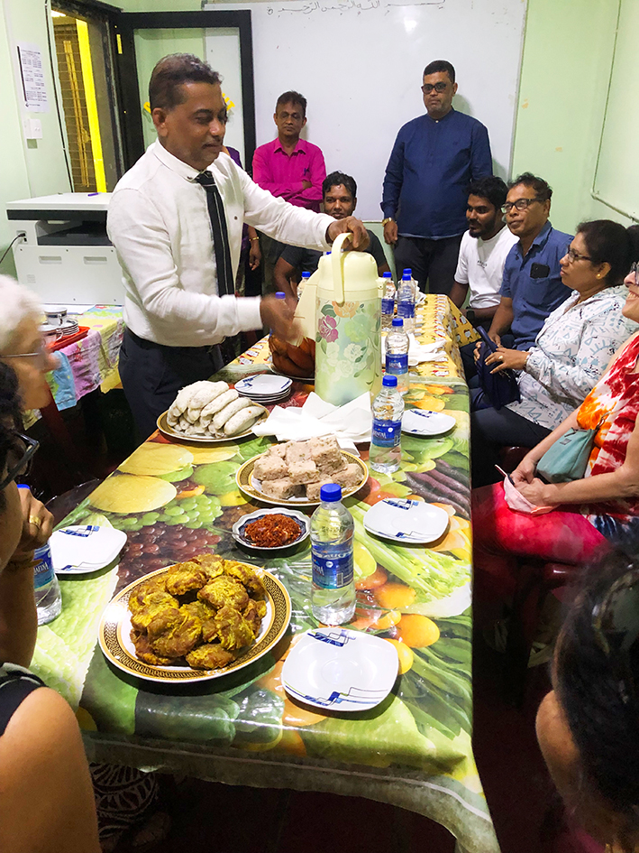Personal des Al-Akram College in Sri Lanka um einen Tisch mit Essen und Getränken